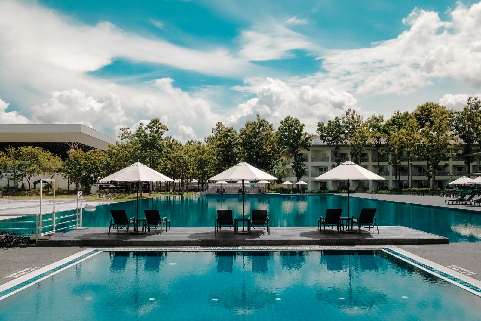 A large, brilliantly blue resort-style pool lined with umbrellas and lounge chairs